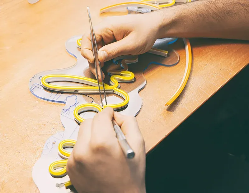 Mãos de artesão montando um letreiro de Neon LED amarelo sobre uma base acrílica